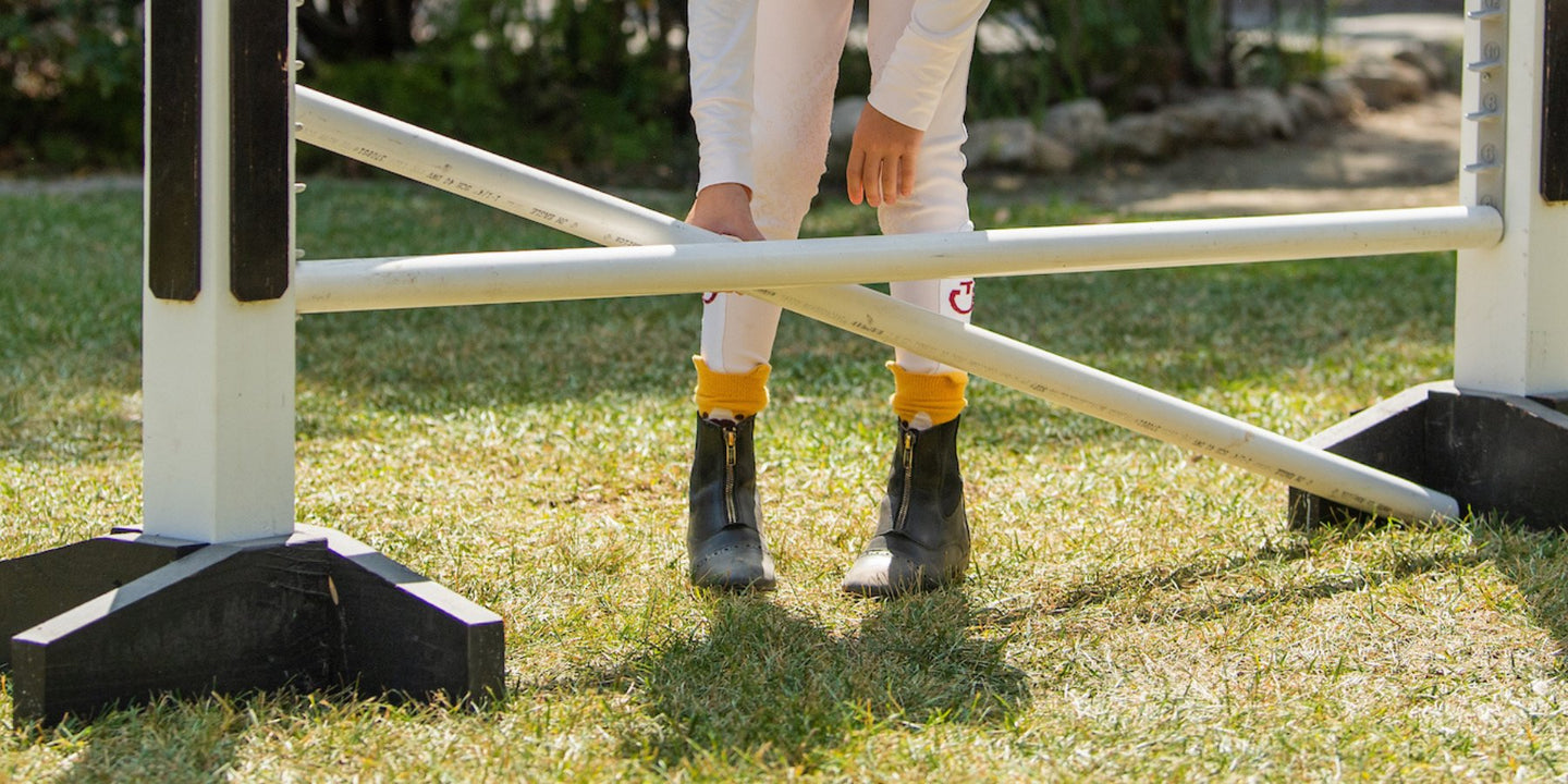 Child horseback rider in breeches and paddock boots at a horse jump
