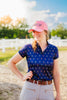 Woman wearing a blue patterned shirt and pink cap with 'Hole Up' text, standing outdoors.