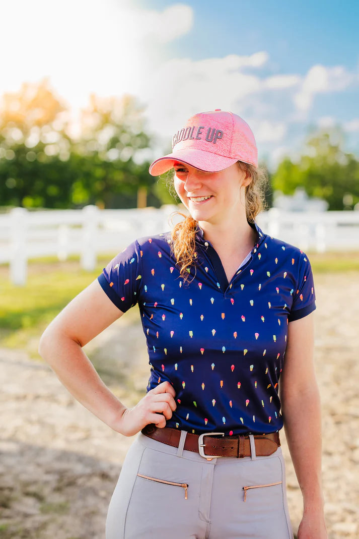 Woman wearing a blue patterned shirt and pink cap with 'Hole Up' text, standing outdoors.